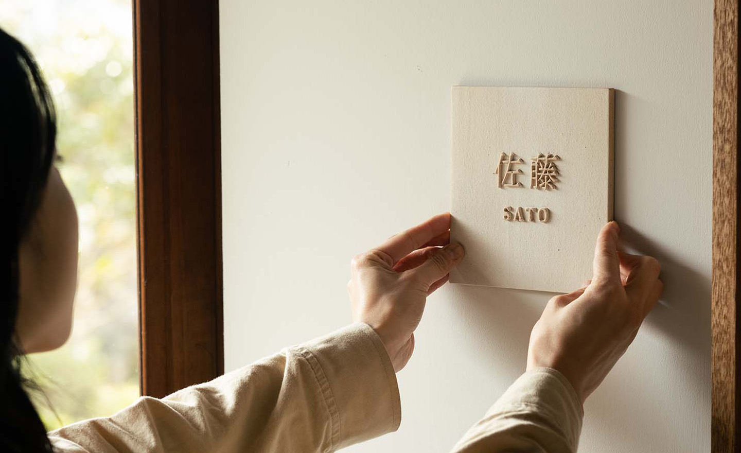シンプルで洗練された印象の信楽焼陶器表札を壁に取り付けるシーン。白い壁にも映える柔らかな風合い