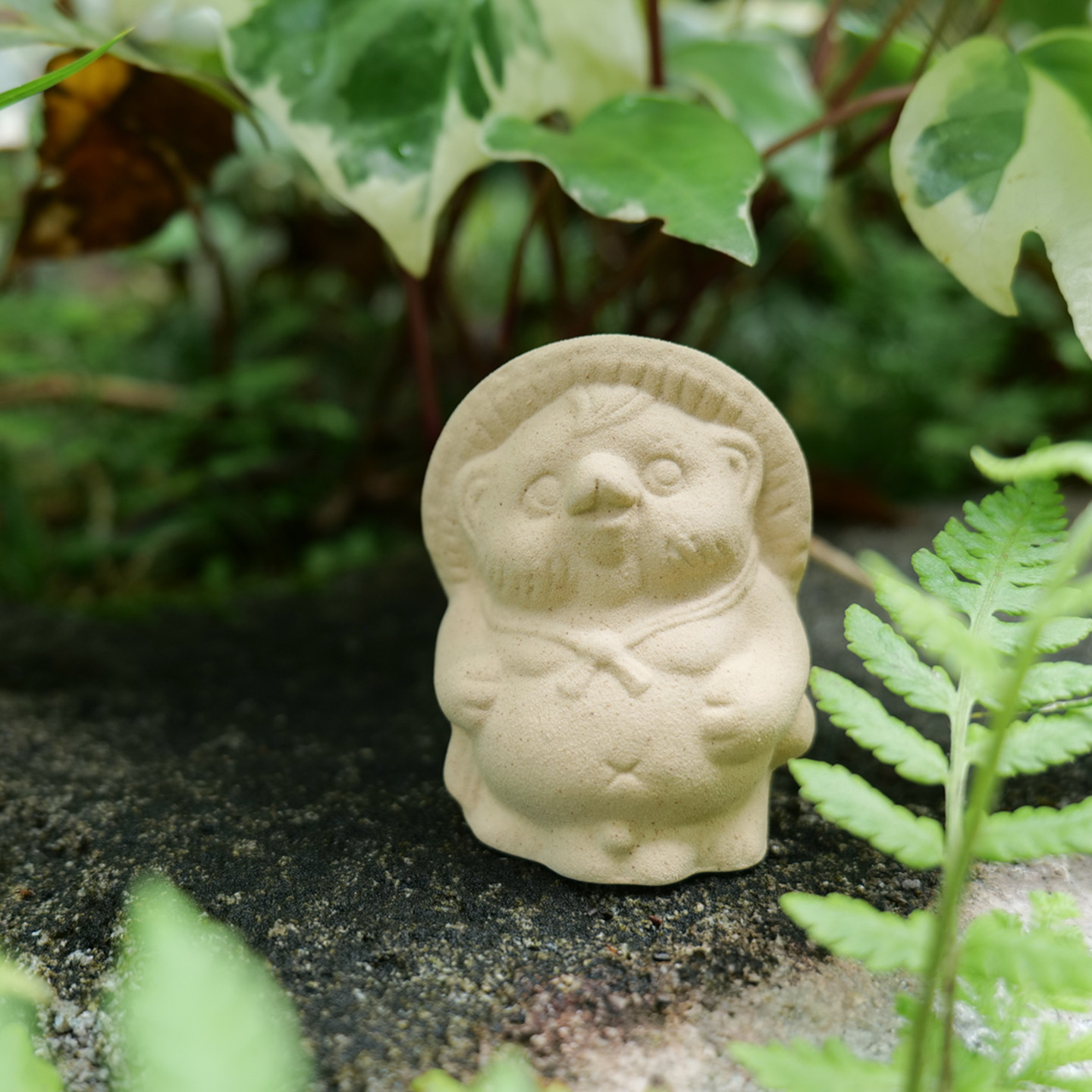 緑の中に佇む陶土のたぬきの置物